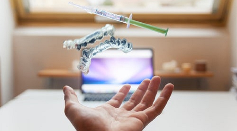 une main , une seringue, un dentier et au loin, un ordinateur allumé